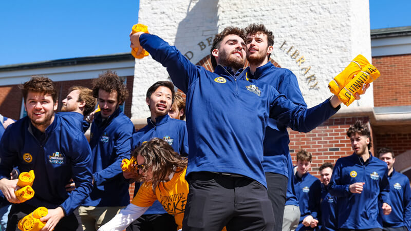 Members of the men's ice hockey team throw rolled up tee shirts from the library steps