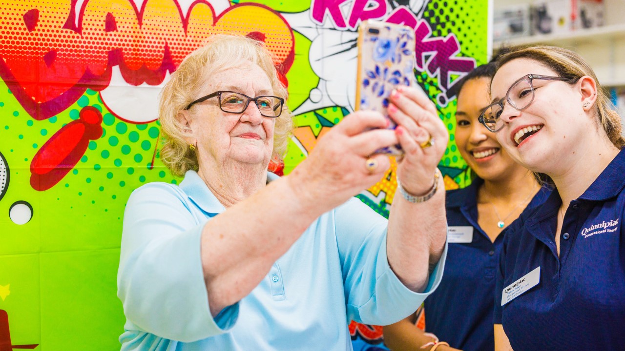 Two OT students teach an older adult how to take a selfie using a cell phone
