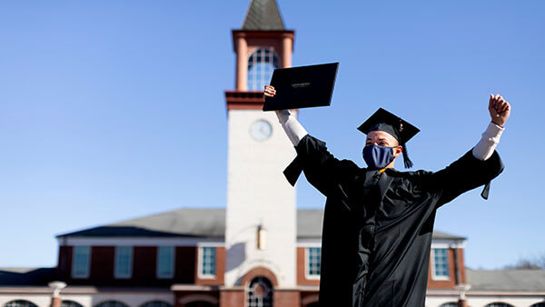 A graduate celebrates wearing his cap and gown on the quad
