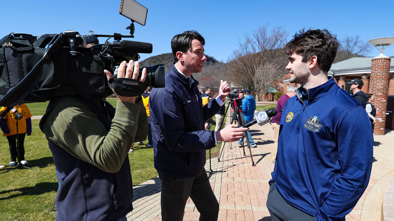 A news station reporter interviews a member of the men's ice hockey team on the quad