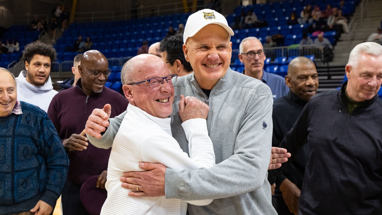 Two men share a hug and smile bright on the M&T Bank Arena basketball court