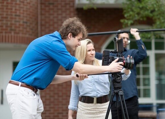 Hardman behind a camera with a female professor watching him and another male holding a microphone boom in the background