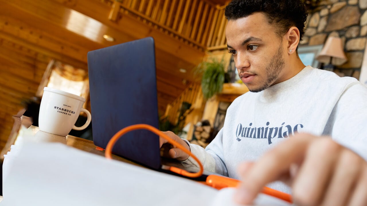 An online student works on his laptop from a coffee shop