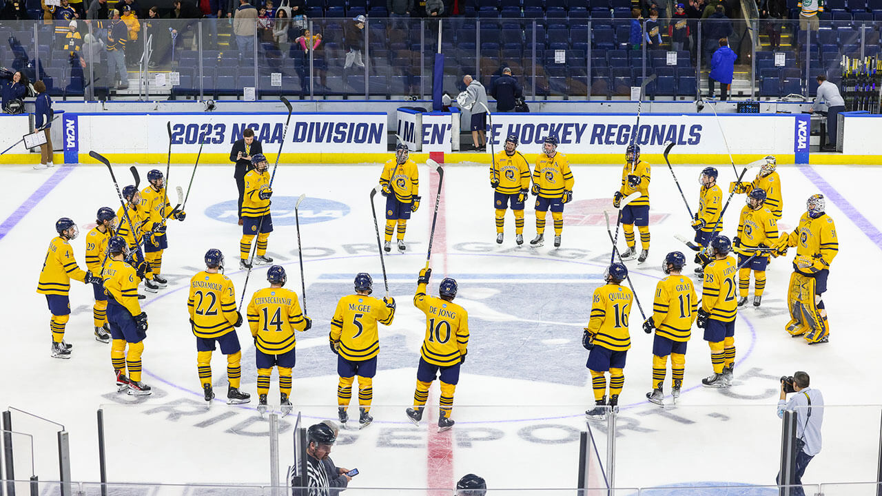The Men's Ice Hockey team stands in a circle on the ice