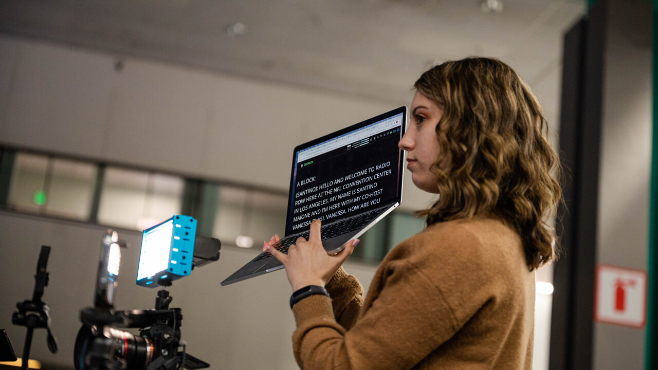 a female student hold a laptop up as a teleprompter