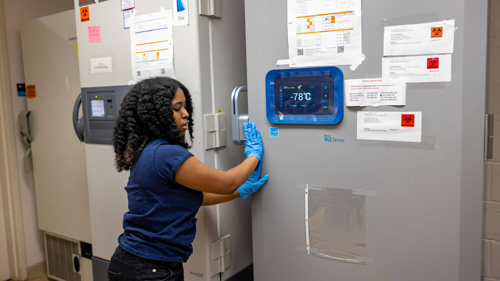 A biology student closes an industrial freezer in a classroom laboratory.