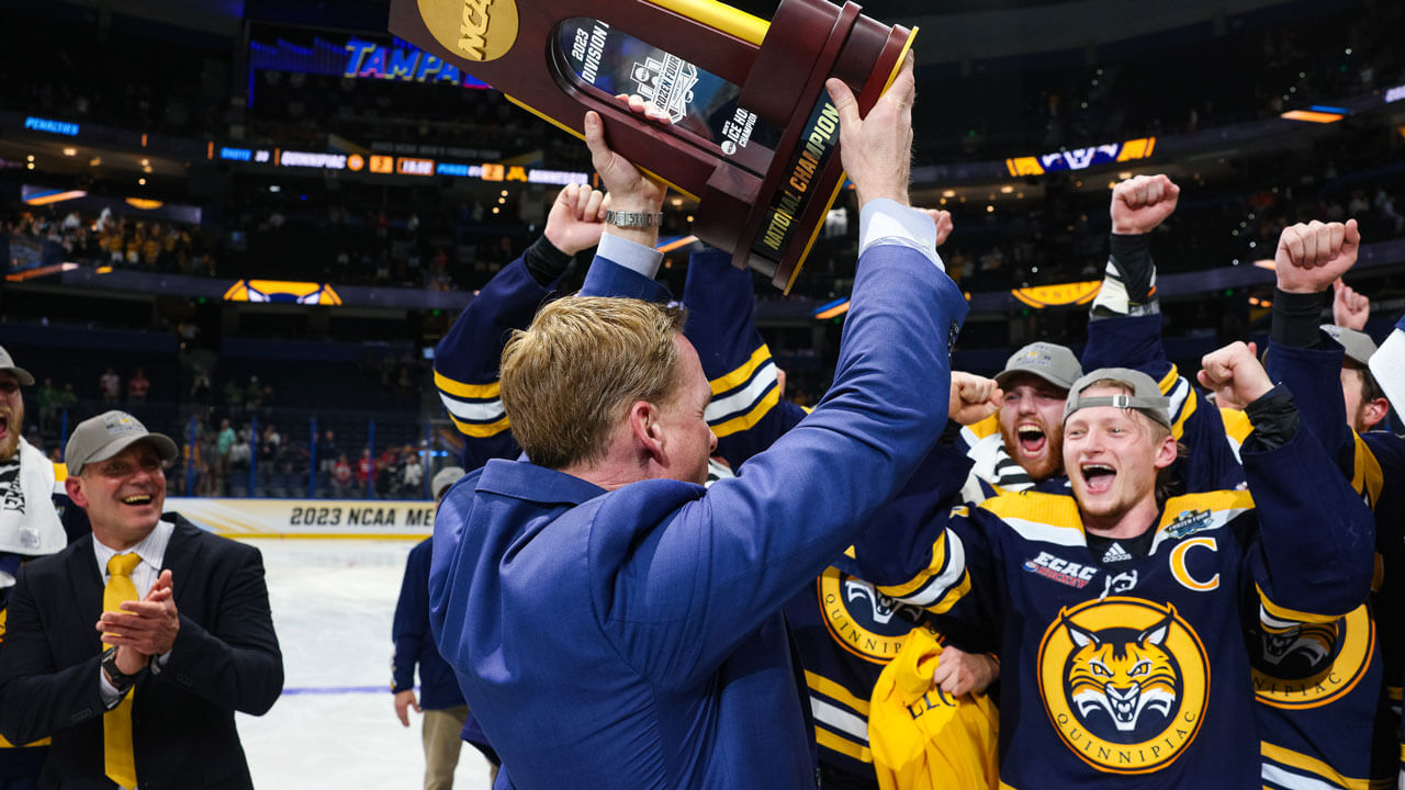 Coach holding up trophy with the hockey team cheering