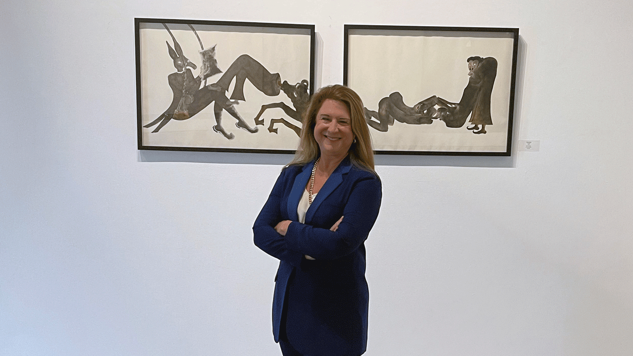 Deborah Colton stands in front of two paintings at her art gallery