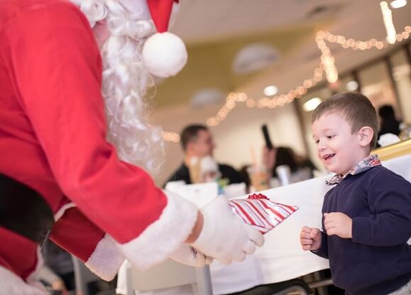 Santa hands a wrapped present to a little boy." title="Health Sciences Santa Party
