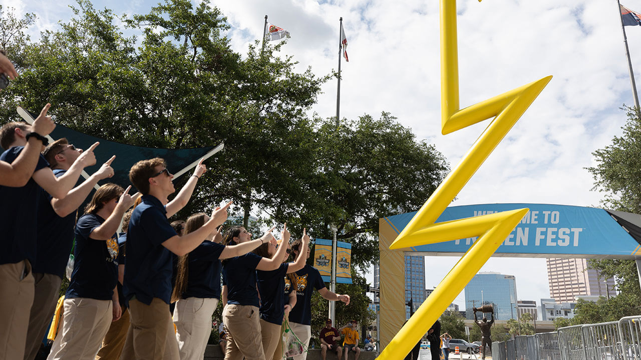 group of pep band members point upwards at the Tampa Lightening statue