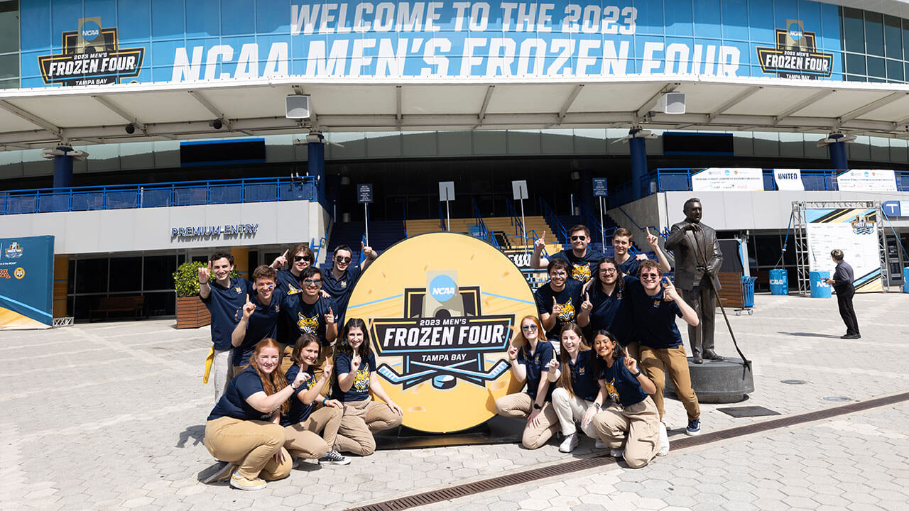pep band poses in front of puck shaped Frozen Four sign, holding up the number one with their fingers
