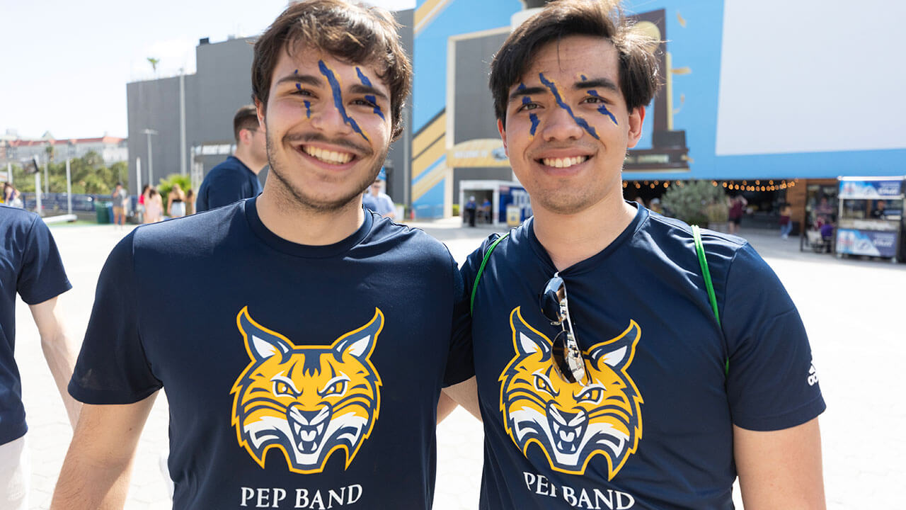 two pep band members pose smiling with blue and gold claw marks across their faces