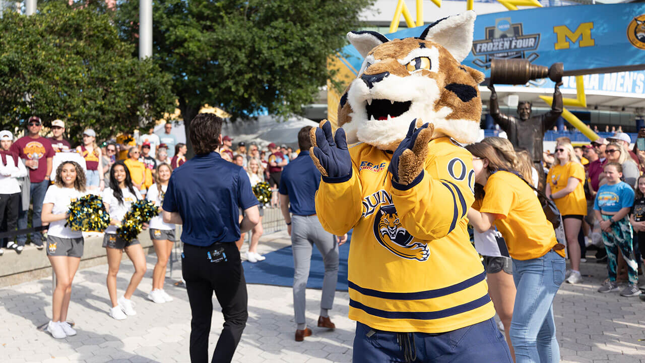 Boomer the bobcat mascot claps for the men's ice hockey team as they walk down the blue carpet