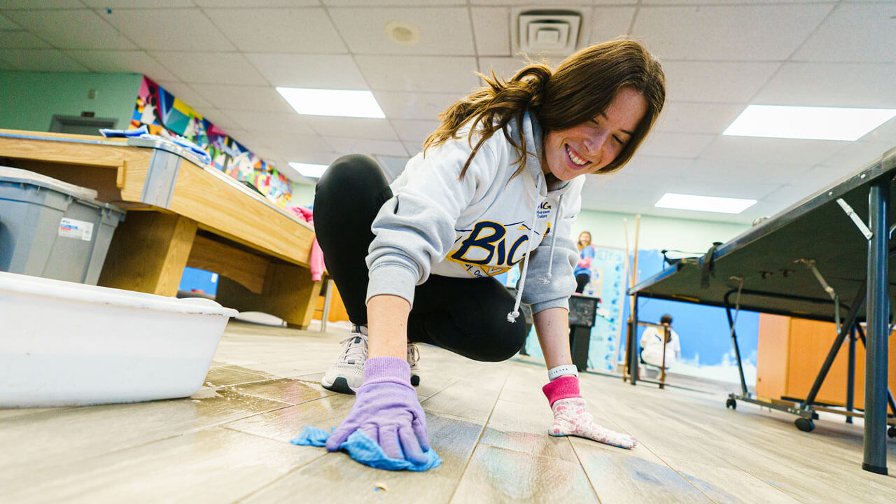 Girl washes floor with a sponge in a classroom during the Big Event