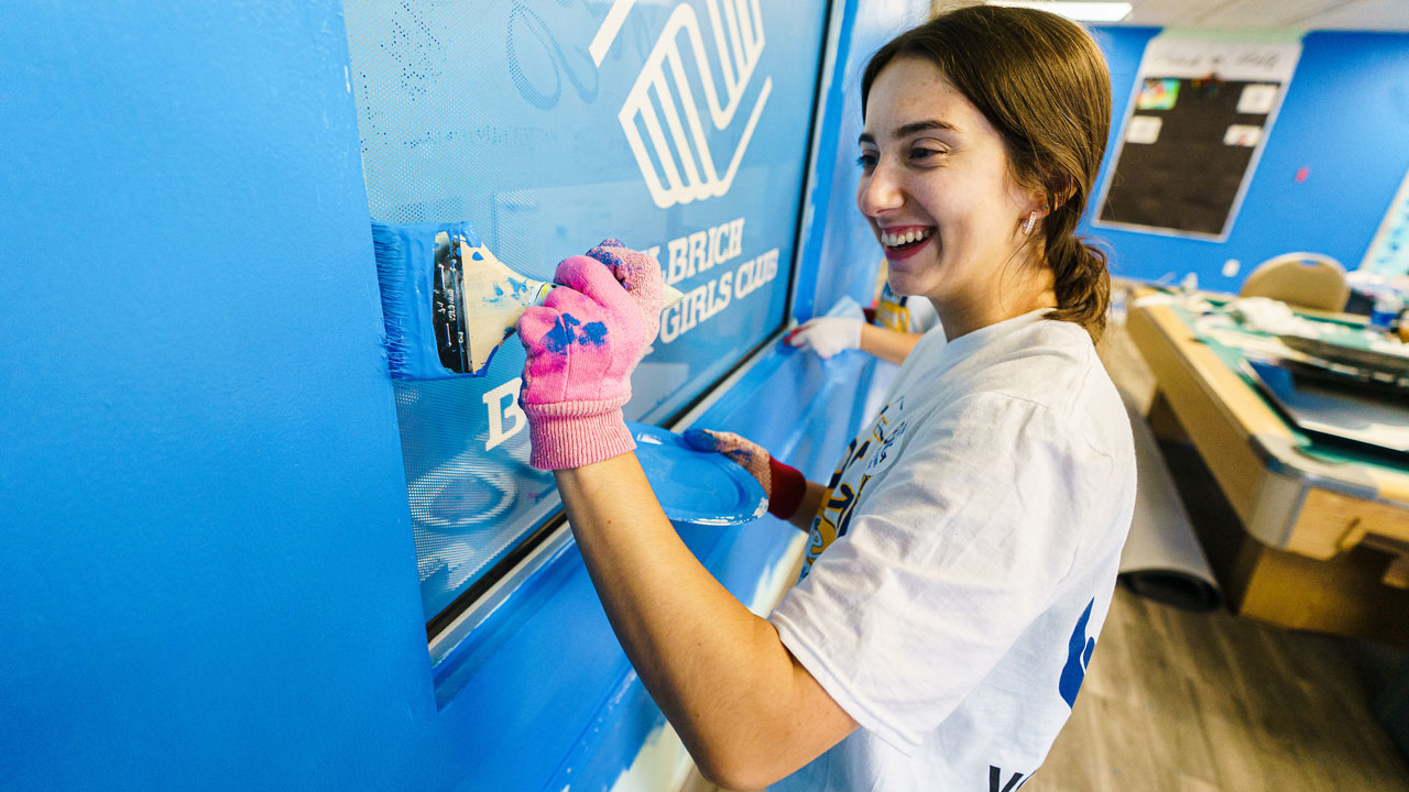 Girl paints a blue wall in a classroom during the Big Event