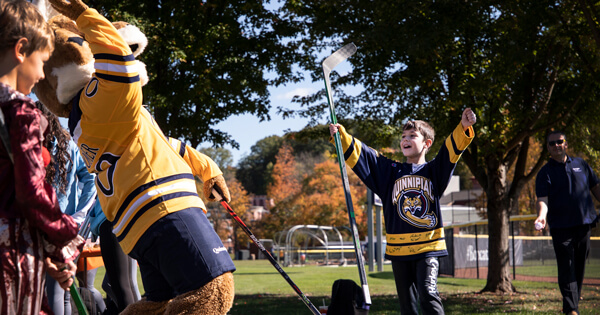 A child cheers with a hockey stick in his hand with Boomer the mascot at Quinnipiac