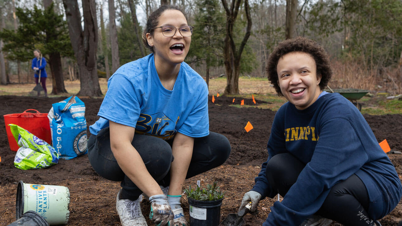 Two girls laughing while shoveling and gardening at the Big Event
