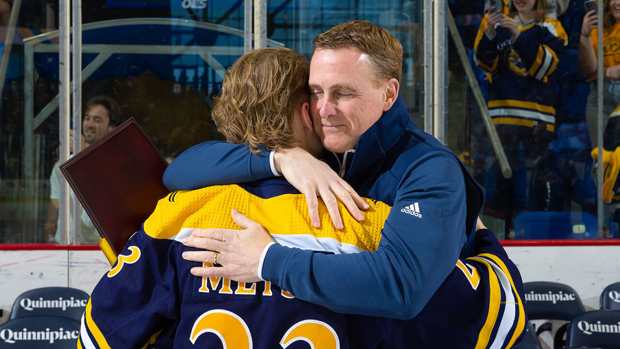 Coach of mens ice hockey team Rand Pecknold hugs player Zach Metsa