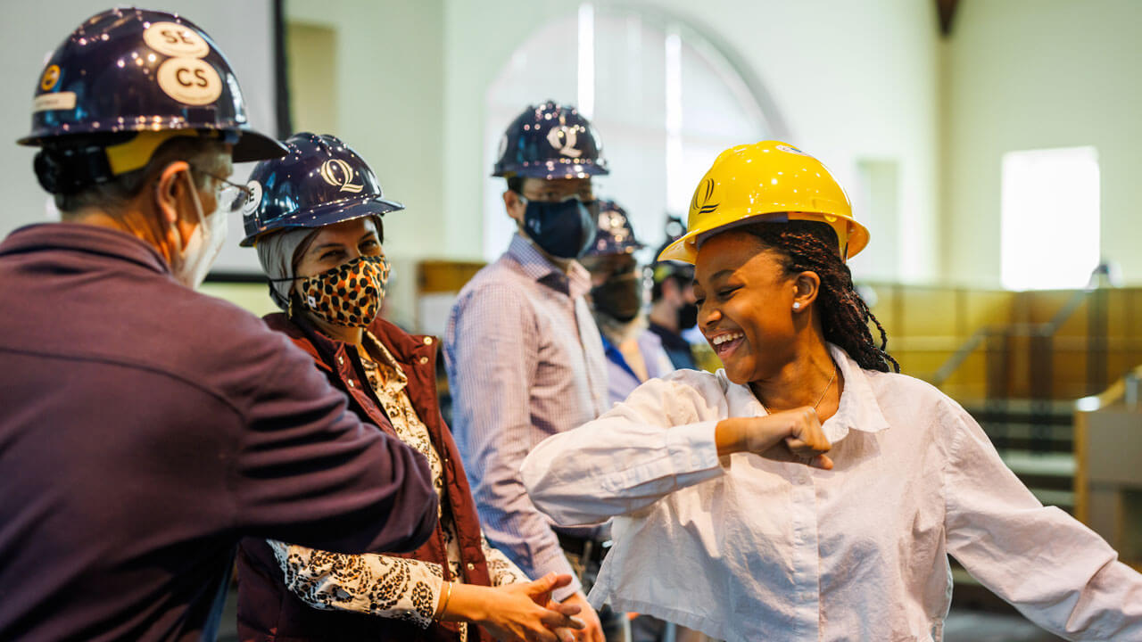 Student elbow-bumping professors and smiling while walking past engineer professors at hard hat ceremony