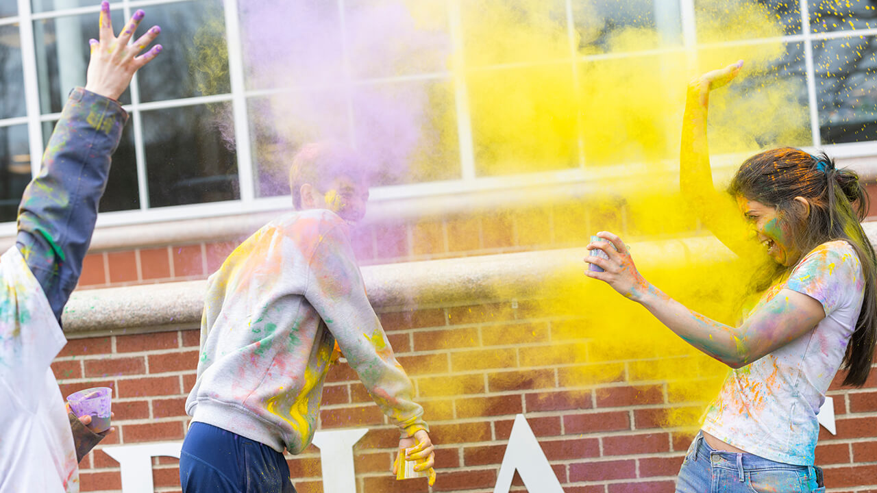 Students throwing yellow and purple powder to celebrate spring