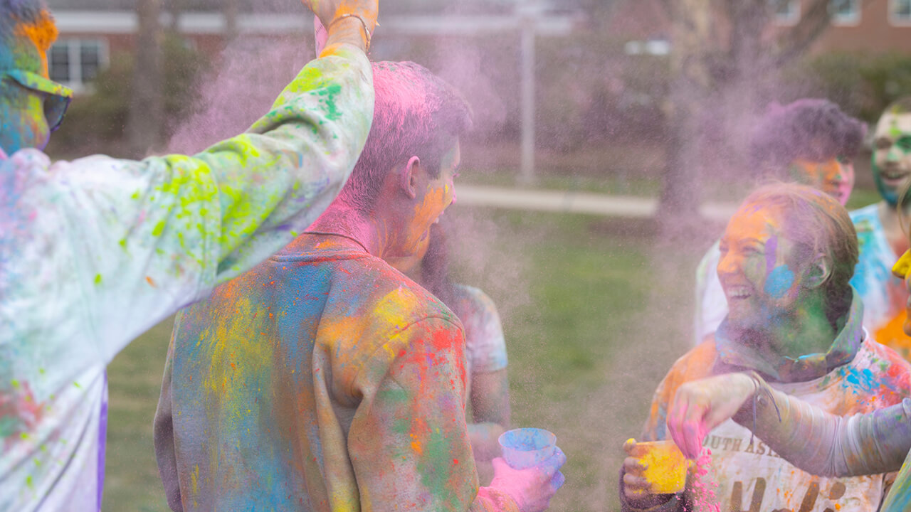 Students covered in different colored paint/powder and laughing at holi celebration