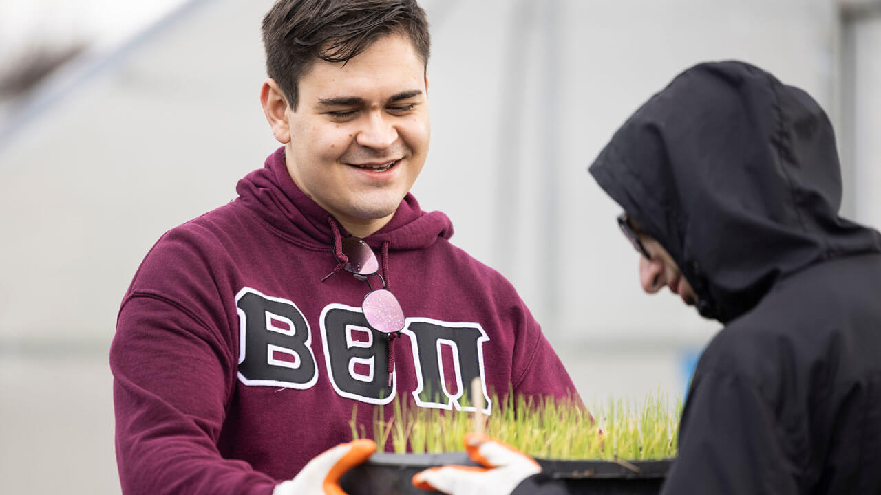 Frat student carries pot of grass while gardening at the Big Event