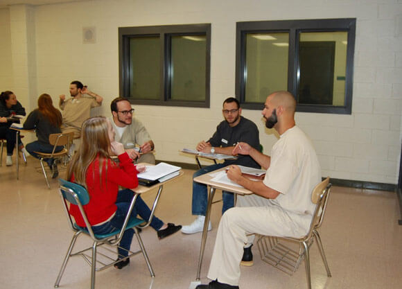 Criminal justice students work with an inmate in a classroom setting at a local prison