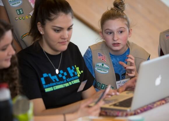 A computer science student helps a troop of girl scouts with building an application on a laptop