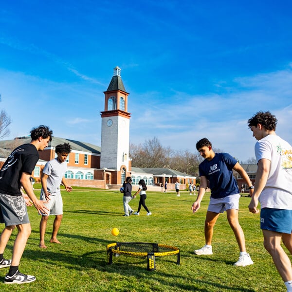 Four students play spikeball on the quad in front of the Arnold Bernhard Library