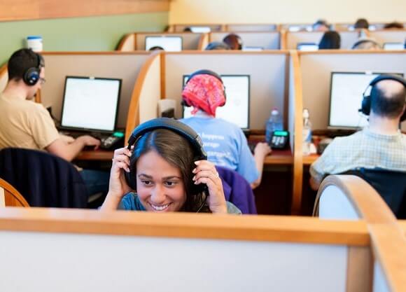 A woman sits with a headset on at the Quinnipiac Polling Institute with a group of people sitting with their backs to her in the background.