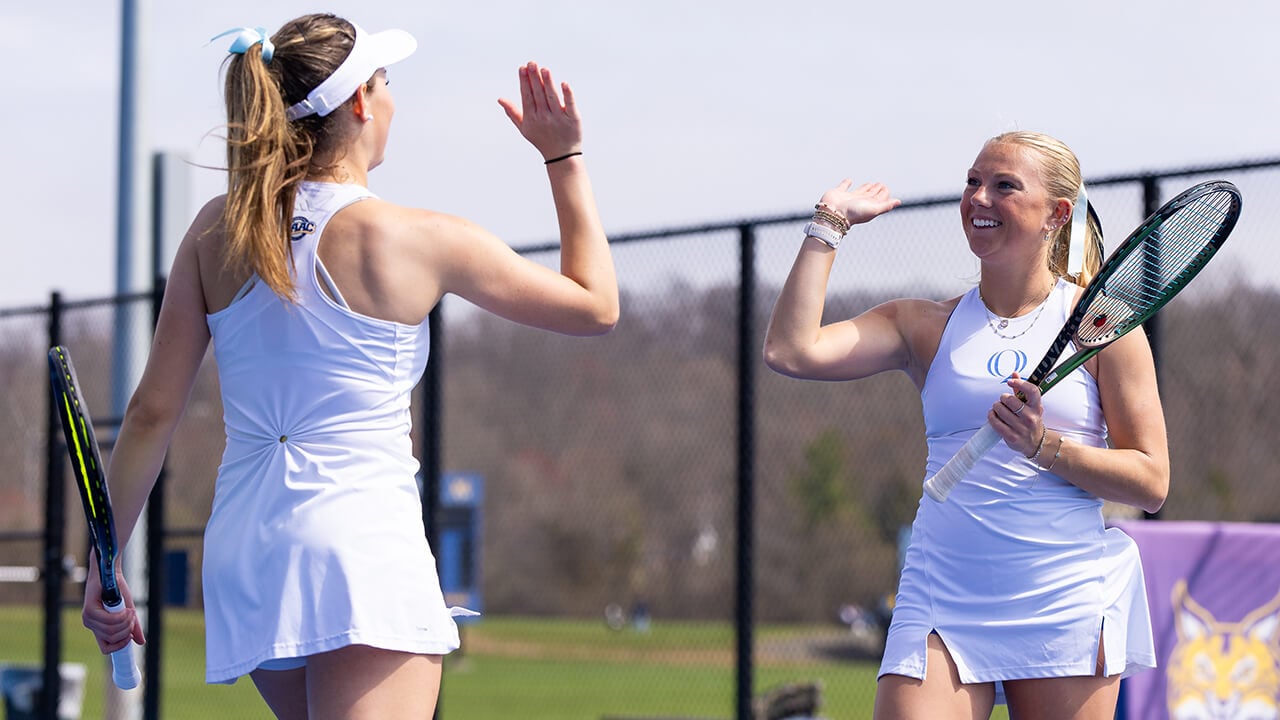Two women's tennis players high-five on the court.