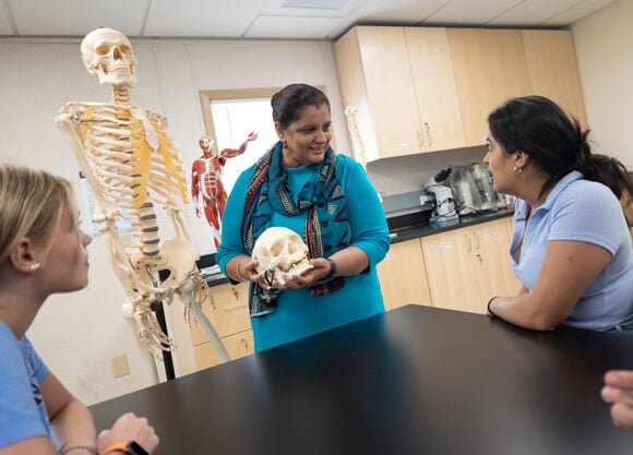 a female professor speaking to 2 female students while holding a skull