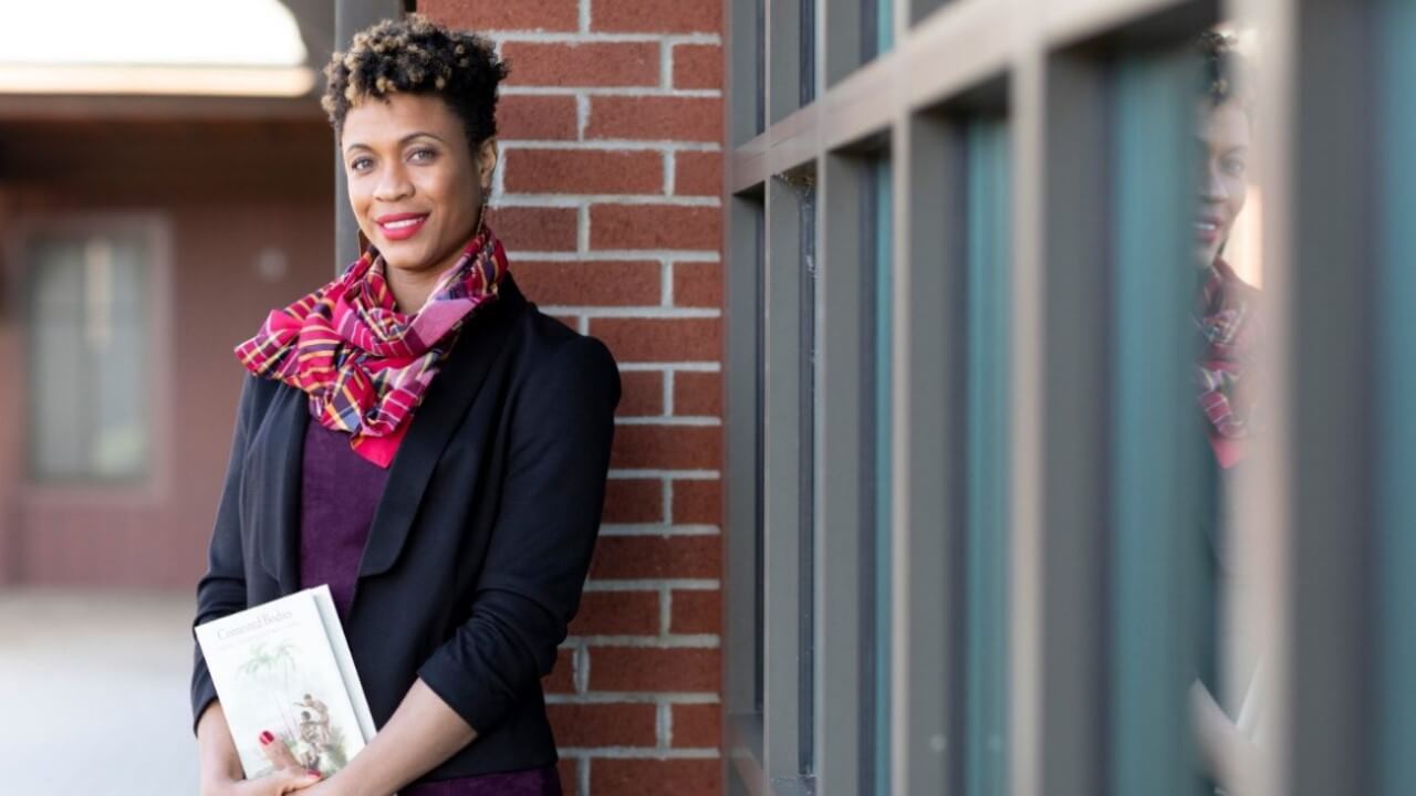 Professor Sasha Turner stands outside Quinnipiac's College of Arts and Sciences holding her book.