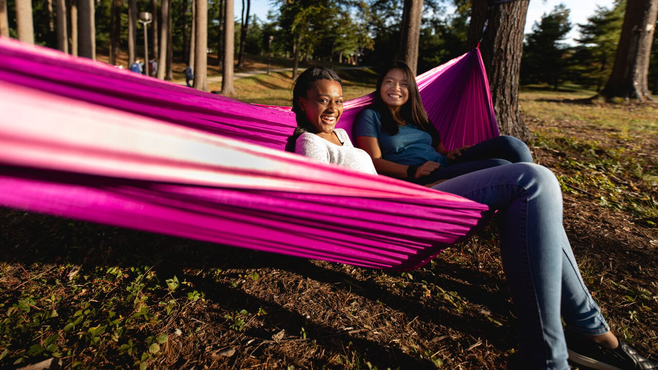 Two students sit in a hammock outside of the College of Arts and Sciences.