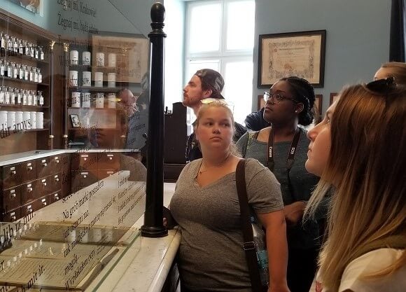 Students stand in a pharmacy from the 1940s looking at displays of glass containers.