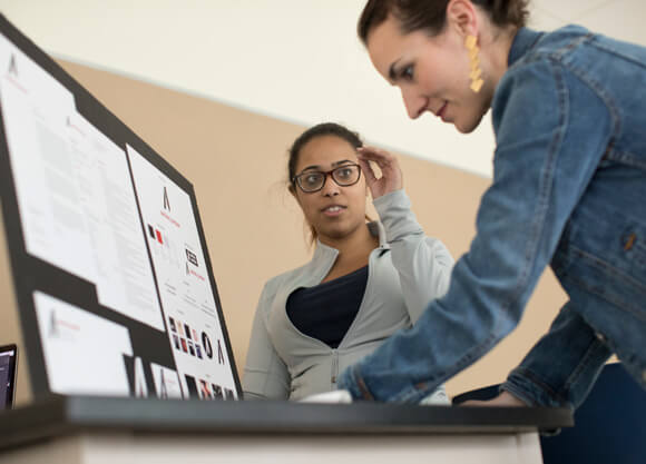 A woman looking at a trifold board with a female student watching