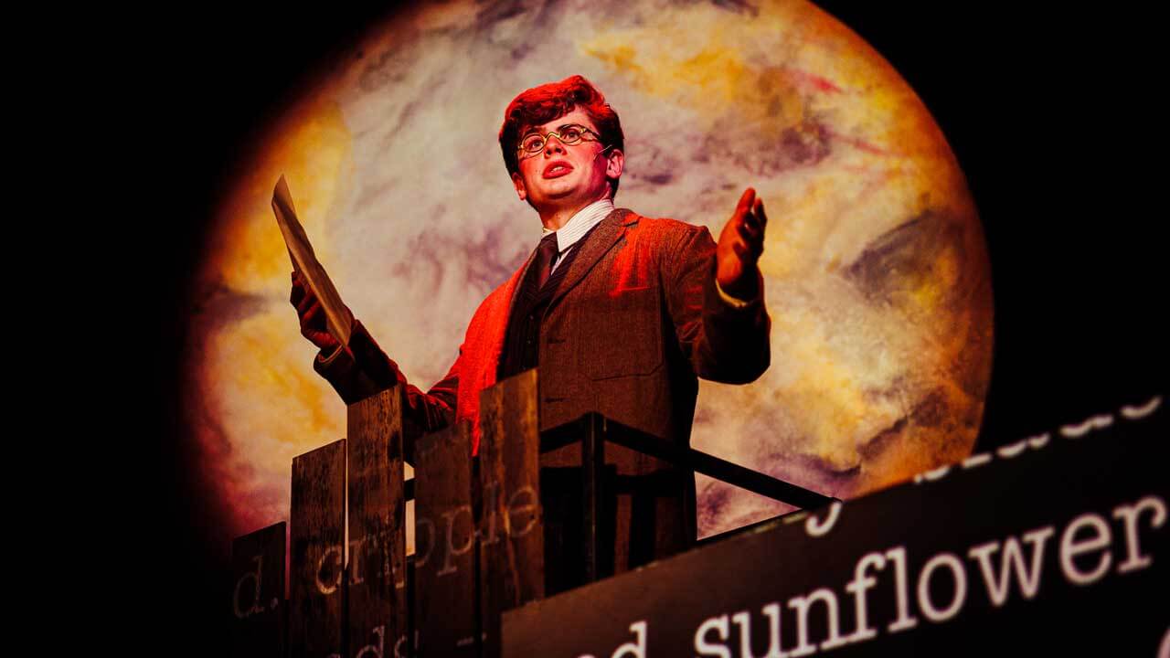 A male student actor on stage in front of a full moon backdrop