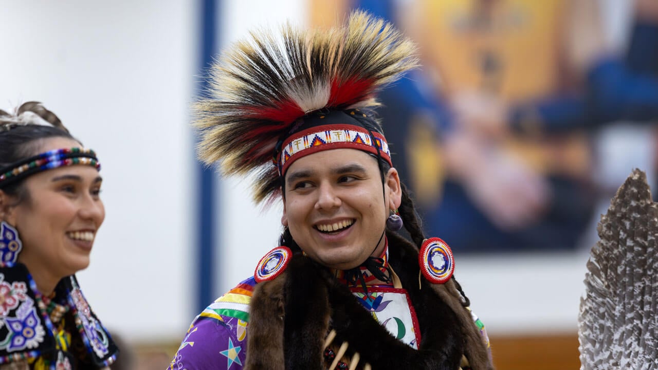 A Powwow dancer in vibrant attire smiles at Quinnipiac’s Dancing in the Shadow of Sleeping Giant Powwow