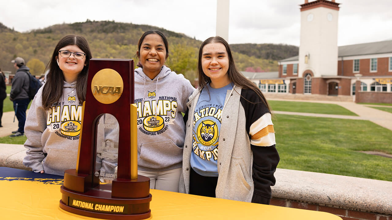 Girls smiling in front of the NCAA National Championship trophy