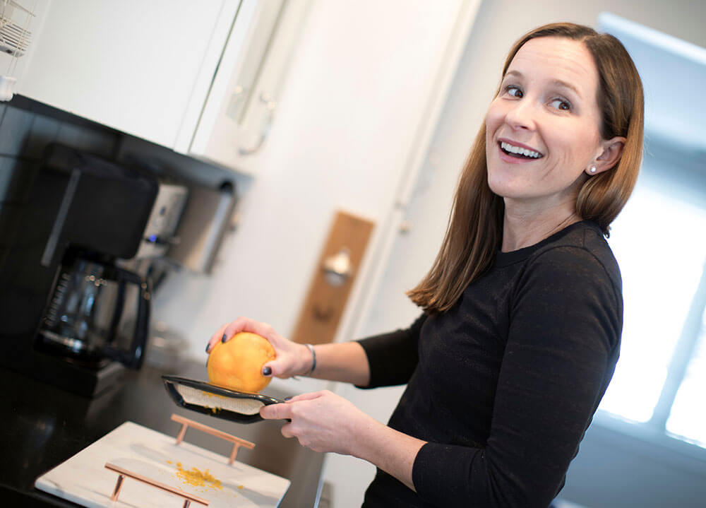 Professor Dana White zests a large orange on a cutting board in a kitchen