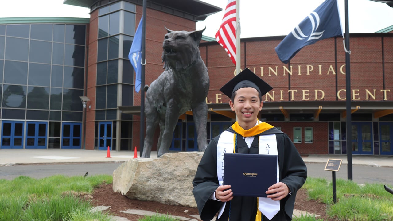 Jayden lee holds diploma in front of bobcat statue