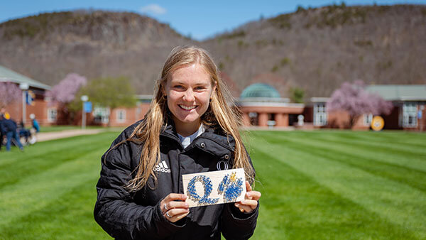 Student Shannon Goria stands on the Quad displaying a Quinnipiac design from her string art business Nailed It!