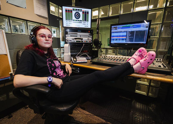 Jen Moglia sitting with legs resting on desk at WQAQ studio