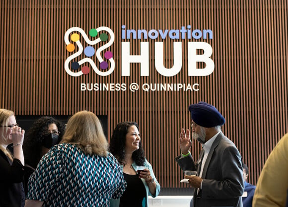 Image of the Innovation Hub sign reading "Innovation Hub Business @ Quinnipiac" with people scattered among the foreground