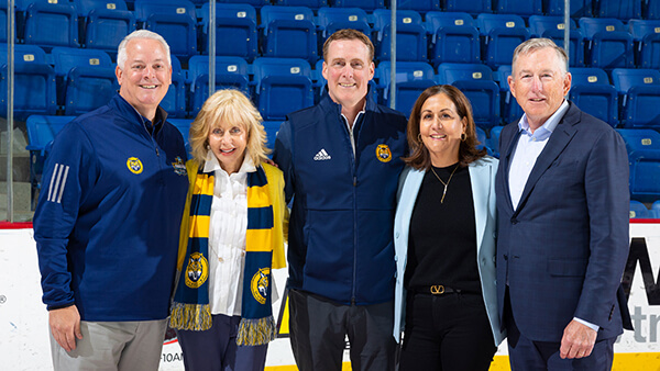 Athletic Director Greg Amodio, President Judy Olian, Men's Ice Hockey Head Coach Rand Pecknold and Jeff and Mimi Kinkead stand in the ice hockey rink at the M&T Bank Arena together.