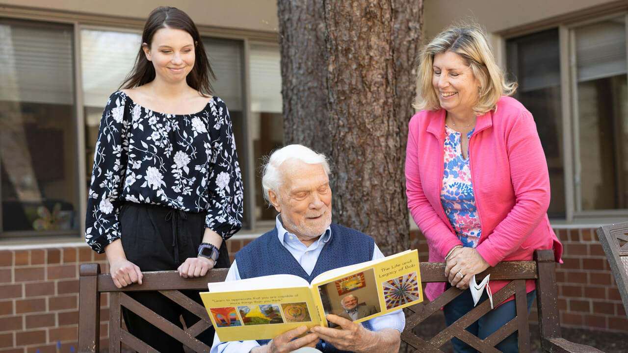 An older man and older women with a student looking at a book