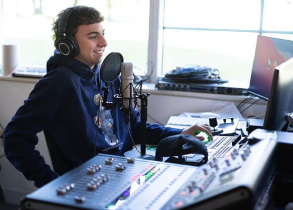 Student smiling and laughing while working at soundboard in the soc podcast studio
