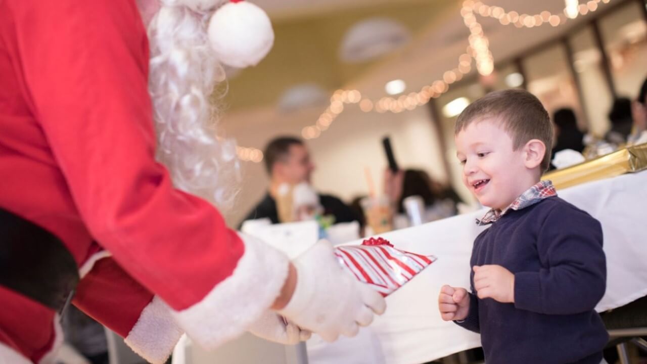 Santa hands a wrapped present to a little boy." title="Health Sciences Santa Party.