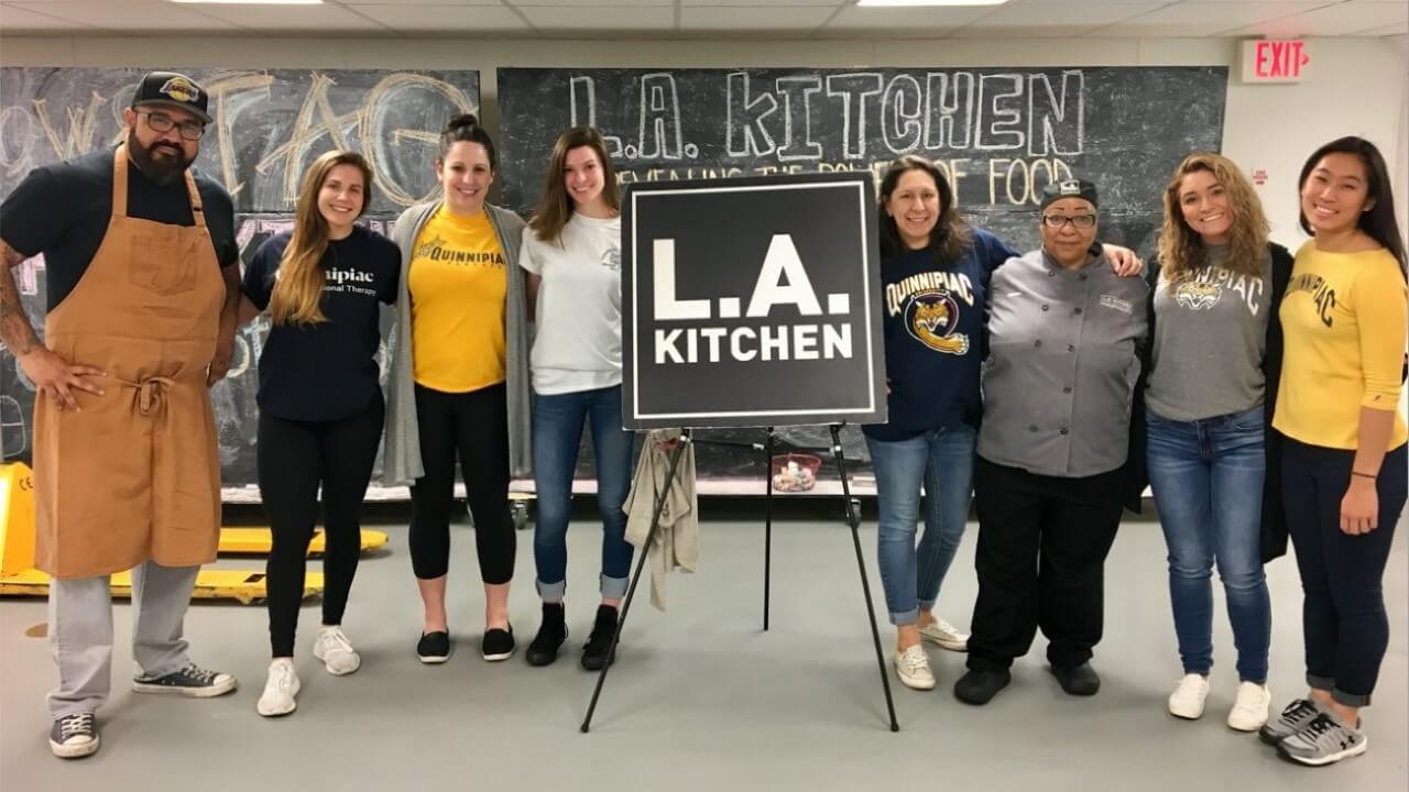 Occupational therapy students arm-in-arm at LA Kitchen in front of a LA Kitchen sign.