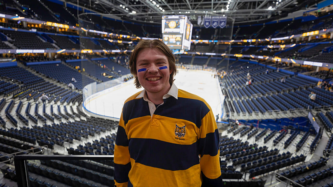 jack gannon, with light brown hair and a pep band yellow and blue striped rugby in front of a hockey arena